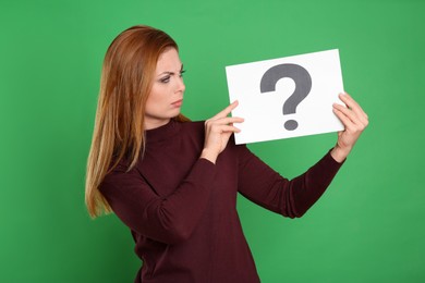 Photo of Confused woman holding question mark sign on green background
