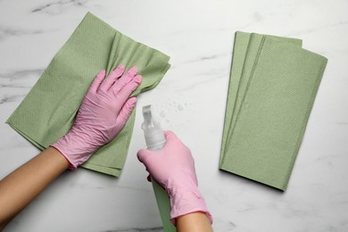 Woman in gloves cleaning light table with paper towel and detergent, top view