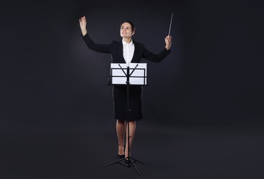 Happy young conductor with baton and note stand on dark background