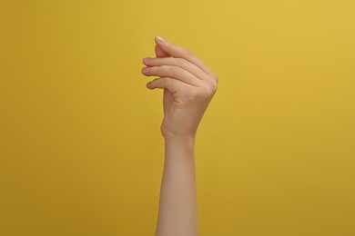 Woman showing thumb and index finger together on yellow background, closeup