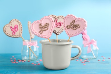 Heart shaped lollipops made of chocolate in cup and sprinkles on light blue background