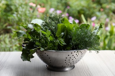 Different herbs in colander on white wooden table outdoors
