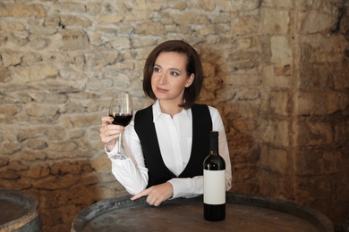 Female sommelier with glass of red wine at table indoors