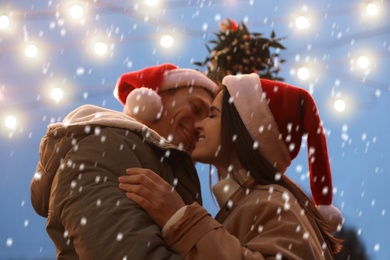 Happy couple kissing under mistletoe bunch outdoors in snowy evening, low angle view