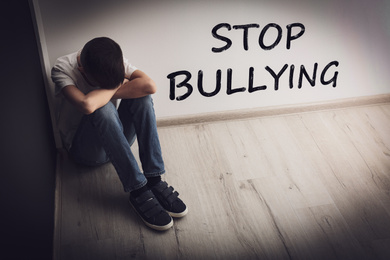 Message STOP BULLYING and upset boy sitting on floor indoors