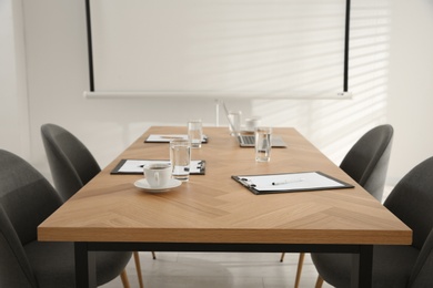 Conference room interior with glasses of water and clipboards on wooden table