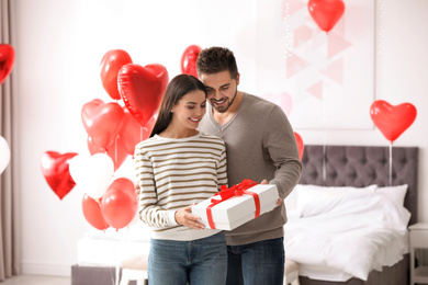 Happy young couple in bedroom decorated with heart shaped balloons. Valentine's day celebration