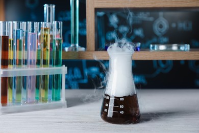 Photo of Laboratory flask and test tubes with colorful liquids on white wooden table. Chemical reaction