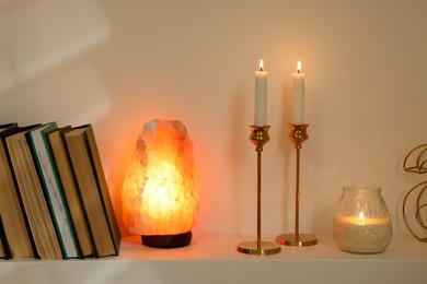 Pair of beautiful candlesticks, scented candle and salt lamp on white shelf