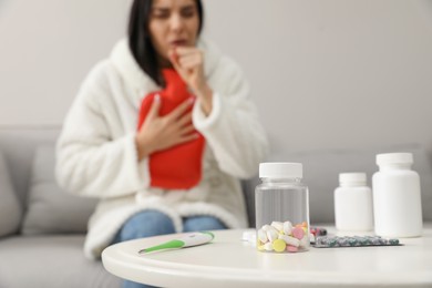 Ill woman with hot water bottle coughing at home, focus on pills