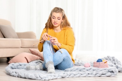 Young woman in cozy warm sweater knitting with needles on floor at home. Space for text