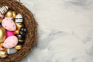 Photo of Decorative nest with many painted Easter eggs on light grey textured table, top view. Space for text