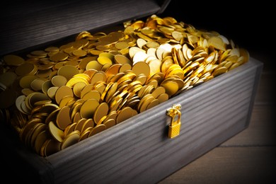 Open treasure chest with gold coins on wooden table, closeup 