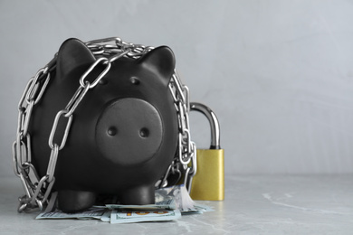 Piggy bank with steel chain, padlock and banknotes on grey marble table, space for text. Money safety concept