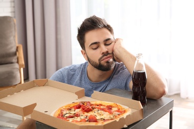 Lazy young man with pizza and drink at home