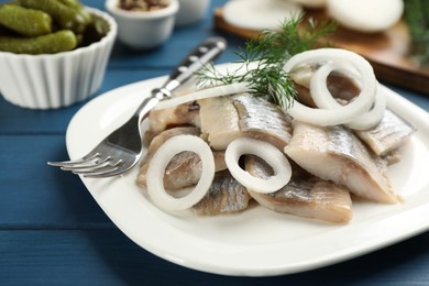 Photo of Plate with sliced salted herring fillet, onion rings and dill on blue wooden table, closeup