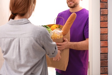 Courier giving paper bag with products to customer at home, closeup. Food delivery service
