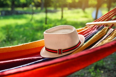 Bright comfortable hammock with hat hanging in green garden, closeup