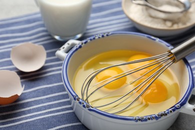 Whisk and eggs in pot on table, closeup