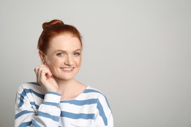 Candid portrait of happy red haired woman with charming smile on light background, space for text