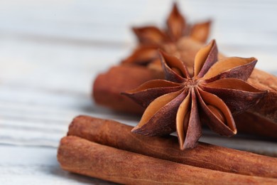 Aromatic anise stars and cinnamon sticks on white wooden table, closeup