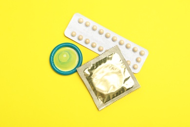 Condoms and birth control pills on yellow background, flat lay. Safe sex concept