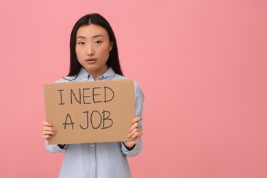Photo of Unemployed Asian woman holding sign with phrase I Need A Job on pink background. Space for text