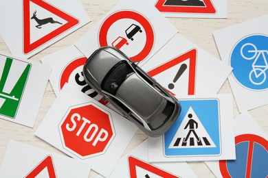 Photo of Cards with different road signs and toy car on white wooden table, flat lay. Driving school