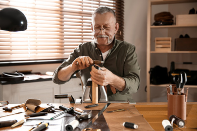 Man burnishing edges of leather belt in workshop