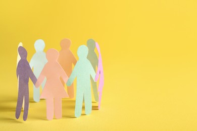Photo of Many different paper human figures standing in circle on yellow background, space for text. Diversity and inclusion concept