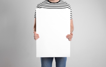 Man holding blank poster on light grey background, closeup