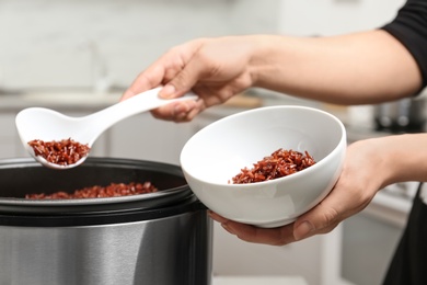 Woman putting brown rice into bowl from multi cooker in kitchen, closeup