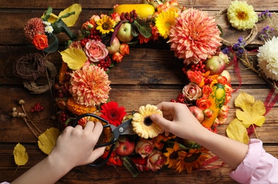 Florist making beautiful autumnal wreath with flowers and fruits at wooden table, top view