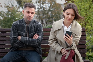 Distrustful man peering into girlfriend's smartphone outdoors. Relationship problems