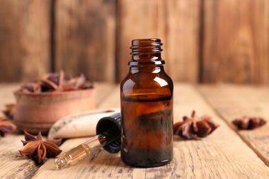 Bottle of essential oil, dropper and anise on wooden table