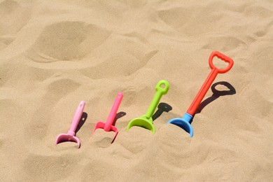 Photo of Bright plastic shovels in sand, space for text. Beach toys