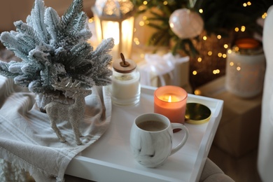 Cup of cocoa, candle and decorative deer on tray at home. Christmas celebration