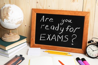 Blackboard with question Are You Ready For Exams? on white table near wooden wall