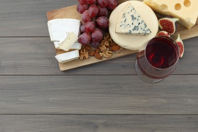 Different types of delicious cheeses, snacks and wine on wooden table, top view. Space for text