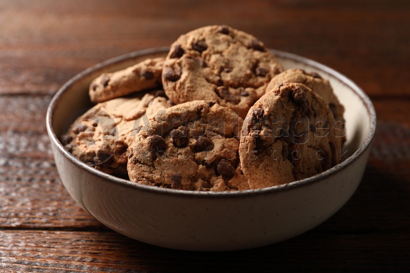 Photo of Delicious chocolate chip cookies in bowl on wooden table
