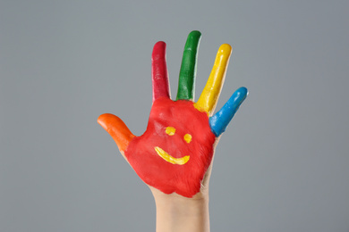 Kid with smiling face drawn on palm against grey background, closeup