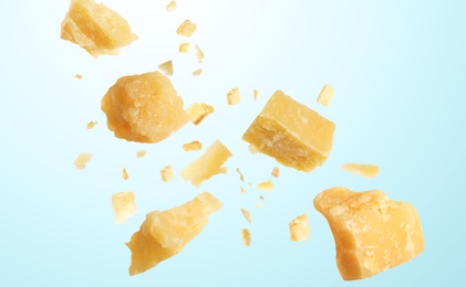 Pieces of delicious parmesan cheese flying on light background