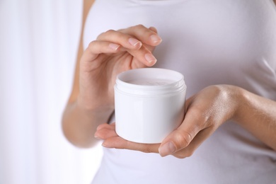 Woman with jar of moisturizing cream on light background, closeup