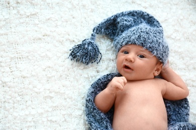 Cute little baby in grey hat and plaid lying on soft blanket, top view. Space for text