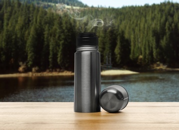 Thermos on wooden table against blurred mountain landscape