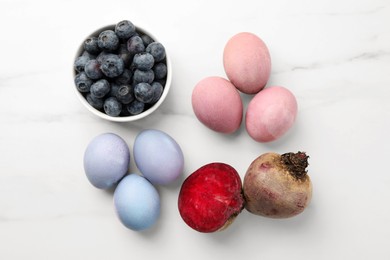 Photo of Colorful Easter eggs painted with natural dyes and ingredients on white marble table, flat lay
