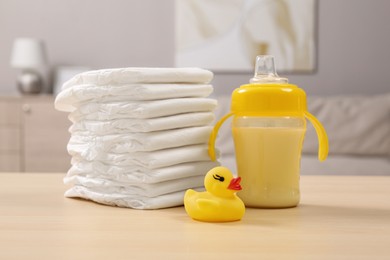 Photo of Stack of diapers, toy duck and baby feeding bottle on wooden table indoors. Maternity leave concept
