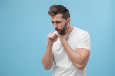 Man coughing on light blue background, space for text. Cold symptoms