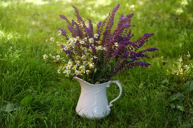 Beautiful bouquet with field flowers in jug on green grass