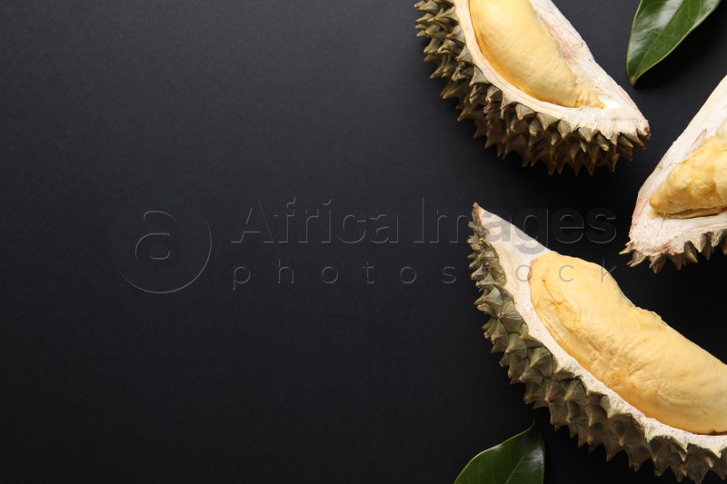 Pieces of fresh ripe durian and leaves on black background, flat lay. Space for text